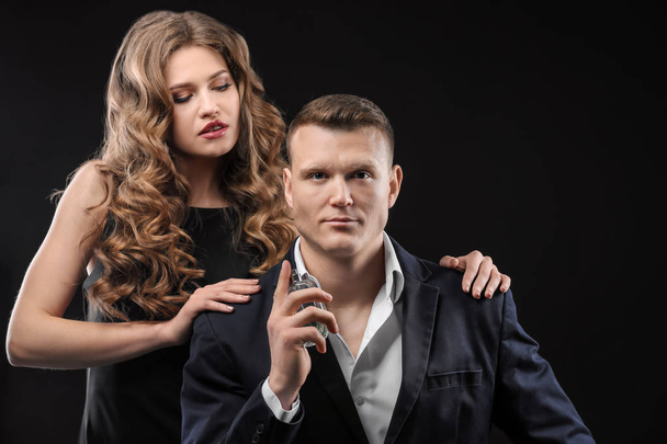 Passionate woman and handsome man using perfume on black background - Foto, afbeelding