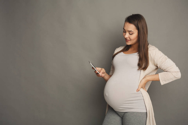 Mosolygó terhes nő használ smartphone - Fotó, kép