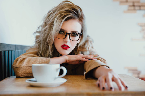 Beautiful fashionable stylish girl sits in a cafe with a cup of coffee. - 写真・画像