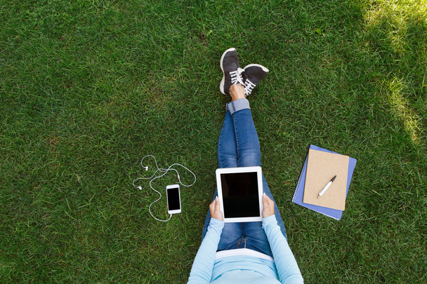 Вид зверху на жінку, що сидить на зеленій траві з планшетом
 - Фото, зображення