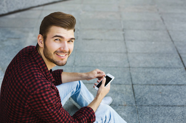Usměvavý mladý muž používající svůj telefon venku - Fotografie, Obrázek