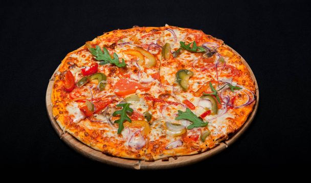 Pizza on a wood board on a black background - Foto, afbeelding