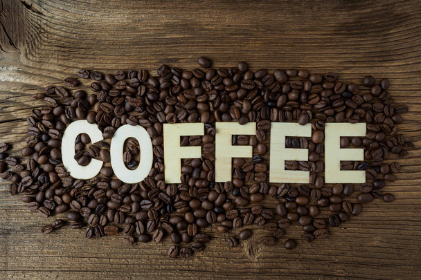 Schwarze Kaffeekörner liegen auf einem braunen Holztisch.  - Foto, Bild