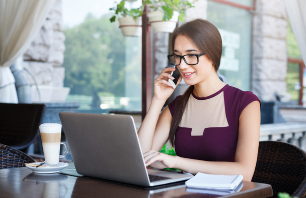 Young businesswoman working on laptop and talking on phone - Photo, Image