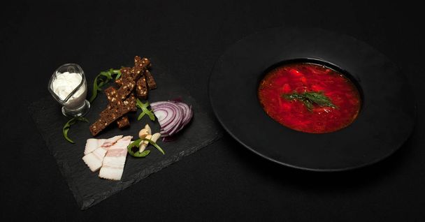 Salted lard with pepper and black bread lies on a plate, next to it there plate with red borsch.. Close-up, top view - Foto, Imagem