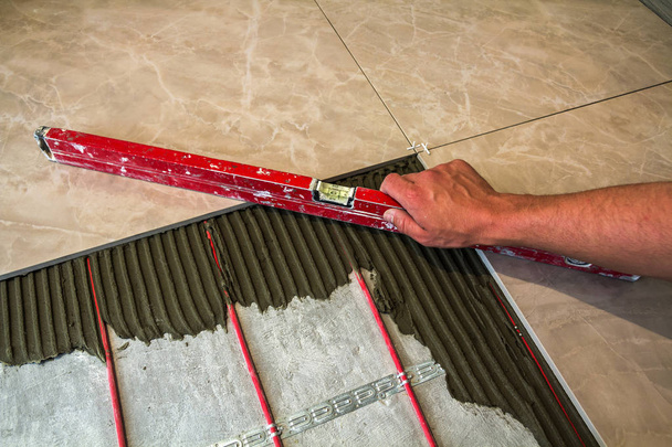 Keramische tegels en hulpmiddelen voor de tegelzetter. Werknemer hand installeren vloer  - Foto, afbeelding