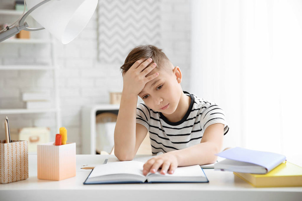 Petit garçon souffrant de maux de tête tout en faisant des devoirs à table à l'intérieur
 - Photo, image
