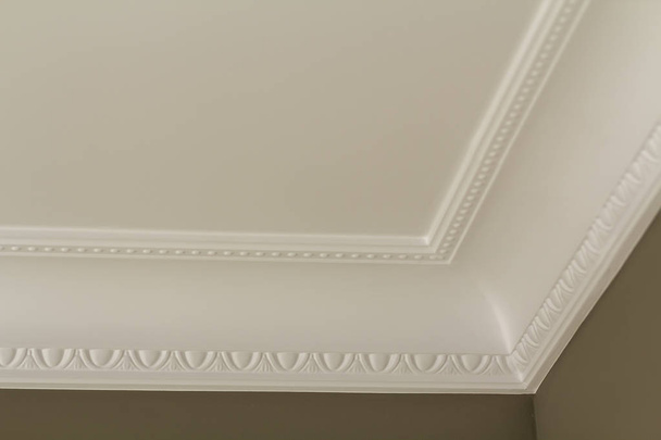 Ornamental white molding decor on ceiling of white room close-up detail. Interior renovation and construction concept. - Фото, зображення