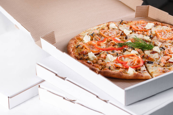 Concepto de entrega de cajas de pizza. Caja abierta con sabrosa pizza italiana en rodajas con salmón, anguila, mariscos, aceitunas, albahaca, tomate, champiñones
. - Foto, Imagen