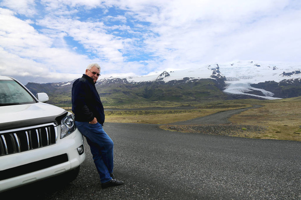 Senior mature confident man standing near SUV car. Scenic mountain landscape on the background. Travel, adventure and endurance concept - Photo, Image