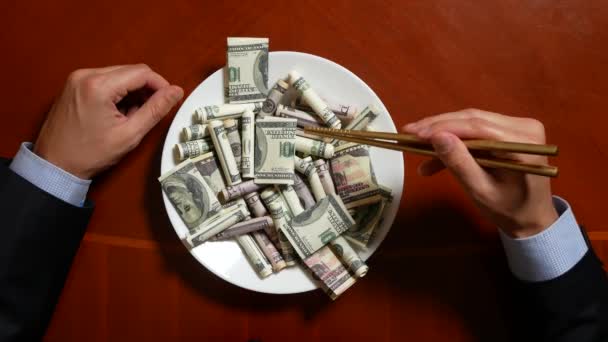 Die Hände eines Geschäftsmannes mit Essstäbchen und Dollarrollen. Dollar essen. 4k. - Filmmaterial, Video