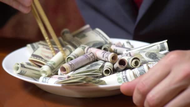 Liikemiehen kädet syömäpuikoilla ja dollarirullilla. Syömässä dollareita 4 k.
. - Materiaali, video