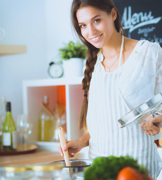 Νεαρή γυναίκα στέκεται δίπλα στη σόμπα στην κουζίνα - Φωτογραφία, εικόνα
