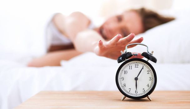 Young sleeping woman and alarm clock in bedroom at home - Фото, зображення