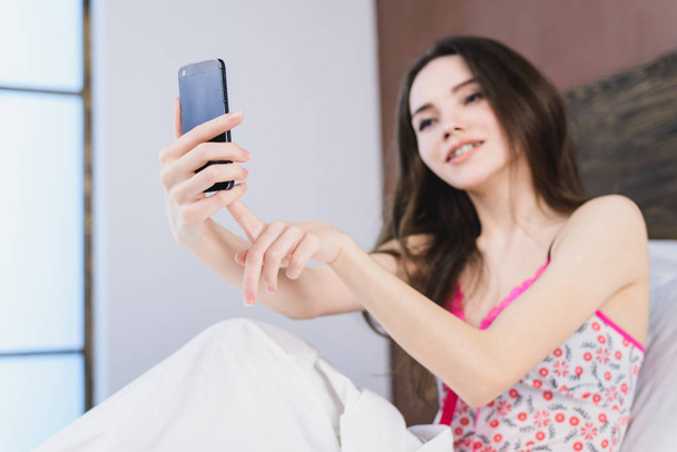 beautiful girl in bed makes selfie on window background - Photo, image