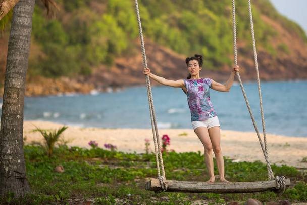 Молода змішана жінка на дерев'яних гойдалках на морському пляжі
. - Фото, зображення