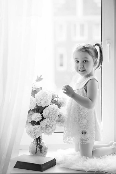 A little girl is sitting on the windowsill. A bouquet of flowers - Fotoğraf, Görsel