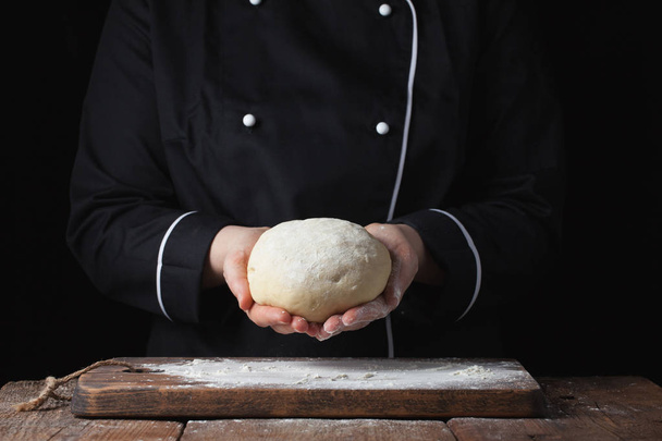 Chef hembra sosteniendo masa de levadura en sus manos sobre fondo negro
 - Foto, Imagen