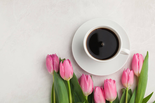 Black coffee in white Cup with pink tulips on light stone background. Top view with copy space - Foto, Bild