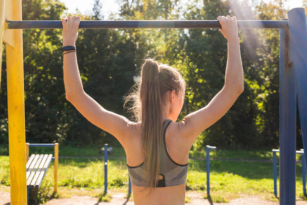 young athletic fitness woman working out at outdoor gym doing pull ups at sunrise. - Fotografie, Obrázek