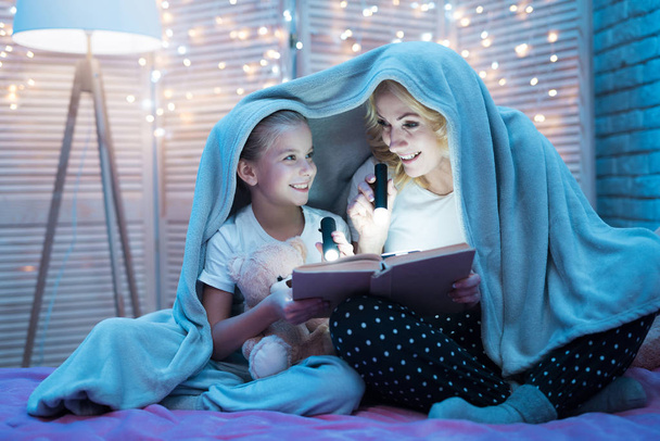 Grandmother and granddaughter reading book under blanket on bed  - Photo, Image