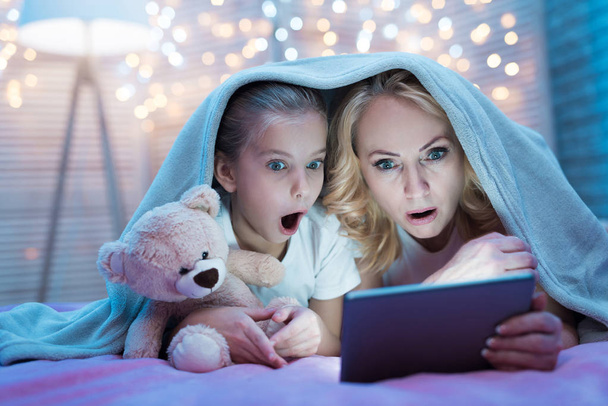 Grandmother and granddaughter watching movie on tablet under blanket on bed at home - Photo, Image