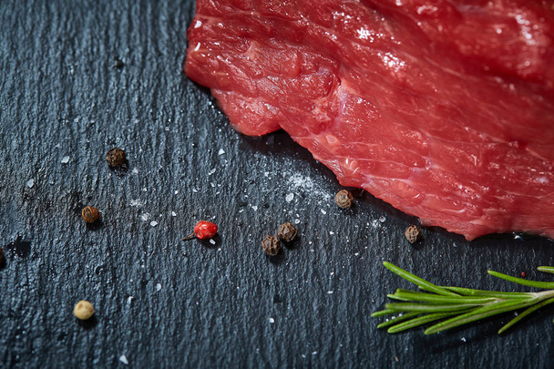 Raw meat beef steaks on black slate board with spices and rosemary, selective focus, shallow depth of field - Foto, imagen