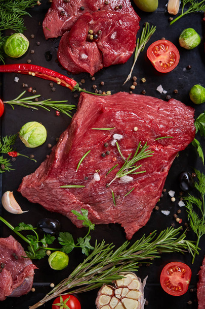 Flat lay of raw beefsteak with vegetables, herbs and spicies on metal tray, close-up, selective focus - Fotografie, Obrázek
