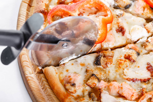 Italian kitchen and cooking concept - cook with cutter cutting pizza to pieces at pizzeria. Hot tasty sliced with salmon, eel, seafood, tomato. - Photo, Image