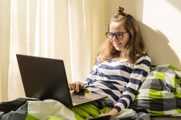 Teenage girl is studying at home, uses laptop in bed - Fotoğraf, Görsel