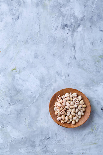 Salted pistachios on a wooden plate over white background, top view, close-up, selective focus. - Fotografie, Obrázek