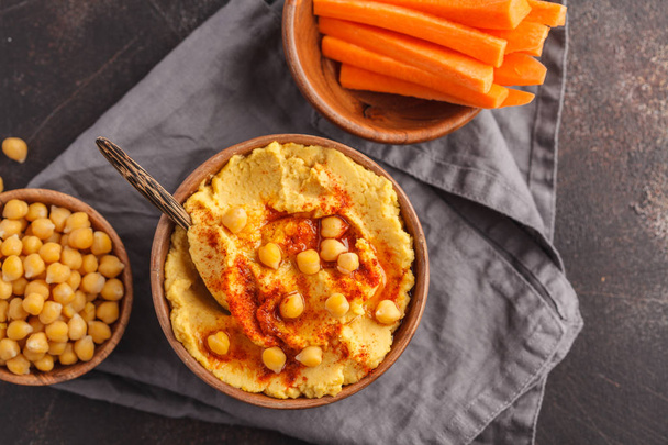 Hummus, fresh carrot sticks and boiled chickpeas in wooden bowls - Photo, image