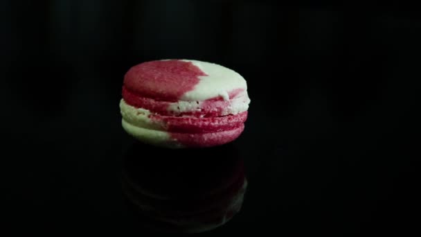 makaronik deser francuski biały i różowy z kremową intercalaire powoli obraca się wokół siebie na czarne lustro backgrond - Materiał filmowy, wideo