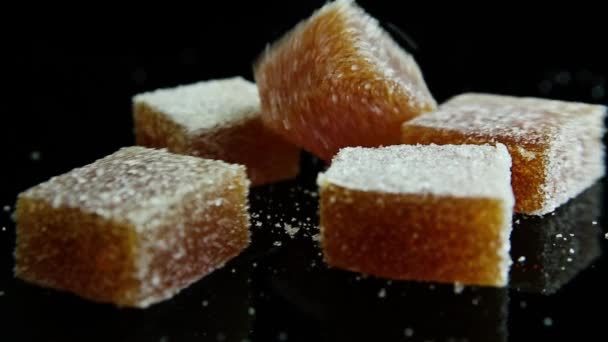Closeup marmelade stukjes vallen op verspreide sinaasappel marmelade groep bedekt met suiker op zwarte spiegel achtergrond - Video
