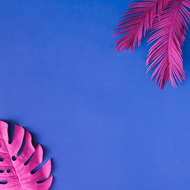 Tropische und Palmenblätter in rosa Farben auf blauem Hintergrund, Konzeptkunst, minimaler Surrealismus  - Foto, Bild