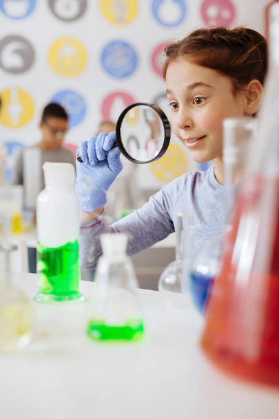 Cute schoolgirl observing chemical reaction through magnifying glass - Фото, зображення