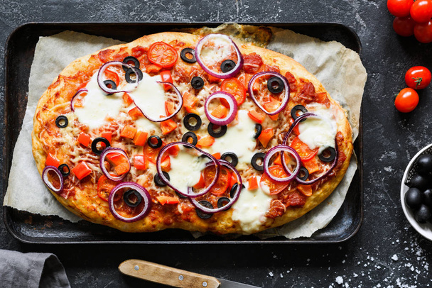 hausgemachte Pizza mit schwarzen Oliven, Zwiebeln, Tomatensauce, Pfeffer und Käse auf Backblech - Foto, Bild