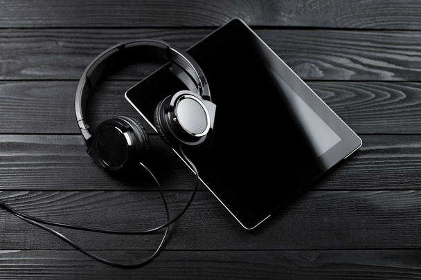 Ψηφιακή δισκίο και τα ακουστικά σε ένα σκοτεινό ξύλινο τραπέζι. - Φωτογραφία, εικόνα