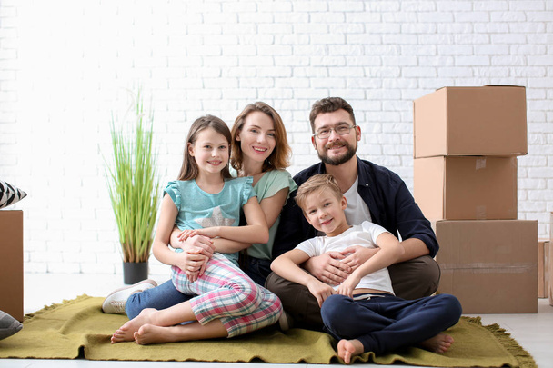 Couple with children sitting near boxes indoors. Happy family on moving day - Zdjęcie, obraz