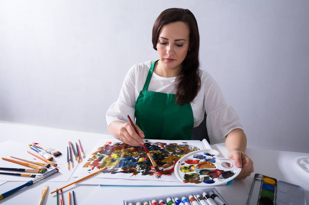Nahaufnahme der Hand einer Künstlerin, die eine Farbpalette hält, während sie auf Leinwandpapier malt - Foto, Bild