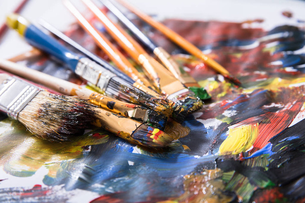 Close-up Of Various Messy Paintbrushes With Multi Colored Paint On Canvas Paper - Foto, afbeelding