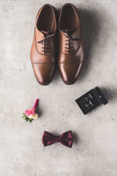 top view of brown shoes, cufflinks, bow tie and boutonniere on gray surface - Photo, Image