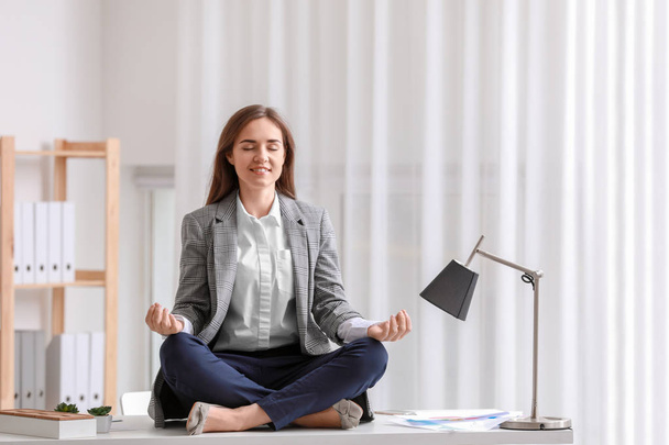 Young woman meditating on table in office - Фото, зображення