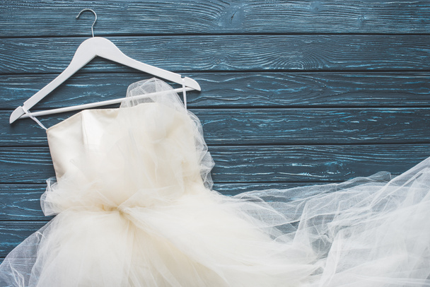 top view of white wedding dress on hanger on wooden dark blue tabletop - Fotoğraf, Görsel