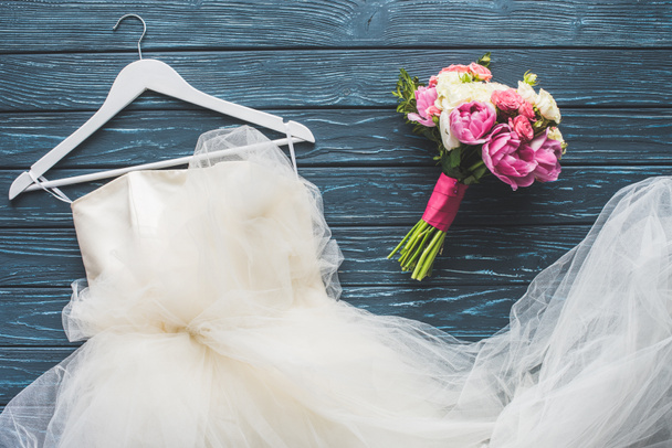 Draufsicht auf Brautstrauß und weißes Kleid auf dunkelblauer Tischplatte - Foto, Bild