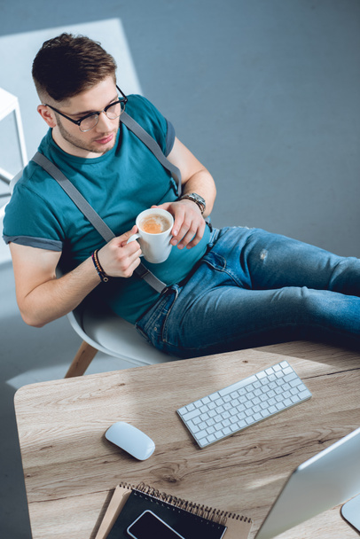 high angle view of young freelancer drinking coffee and working at home office  - 写真・画像
