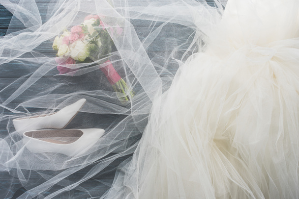 top view of pair of shoes, wedding dress and bouquet on wooden dark blue tabletop - 写真・画像