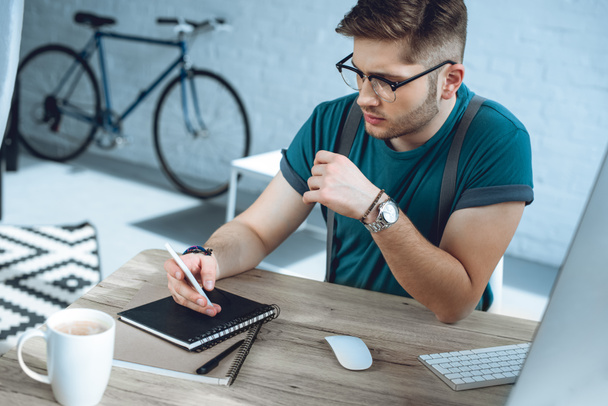 young man in eyeglasses using smartphone while working at home office - Photo, Image