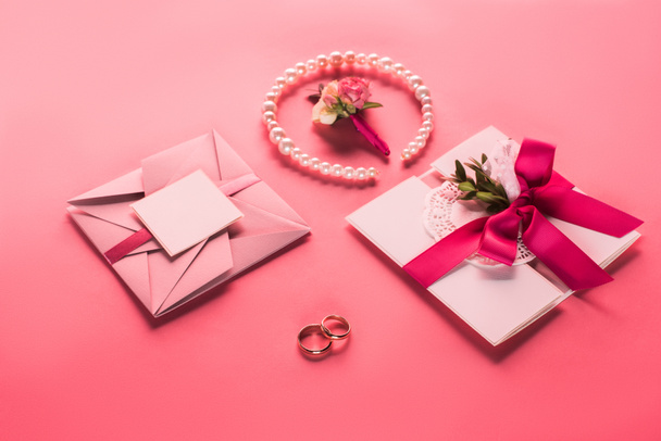 obrączki ślubne, perłowy naszyjnik, boutonniere i różowy koperty z zaproszenia na powierzchni różowy - Zdjęcie, obraz