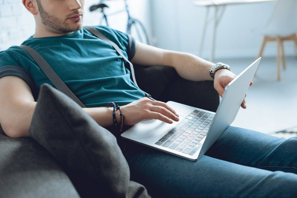 cropped shot of young man using laptop while sitting on couch - Фото, изображение